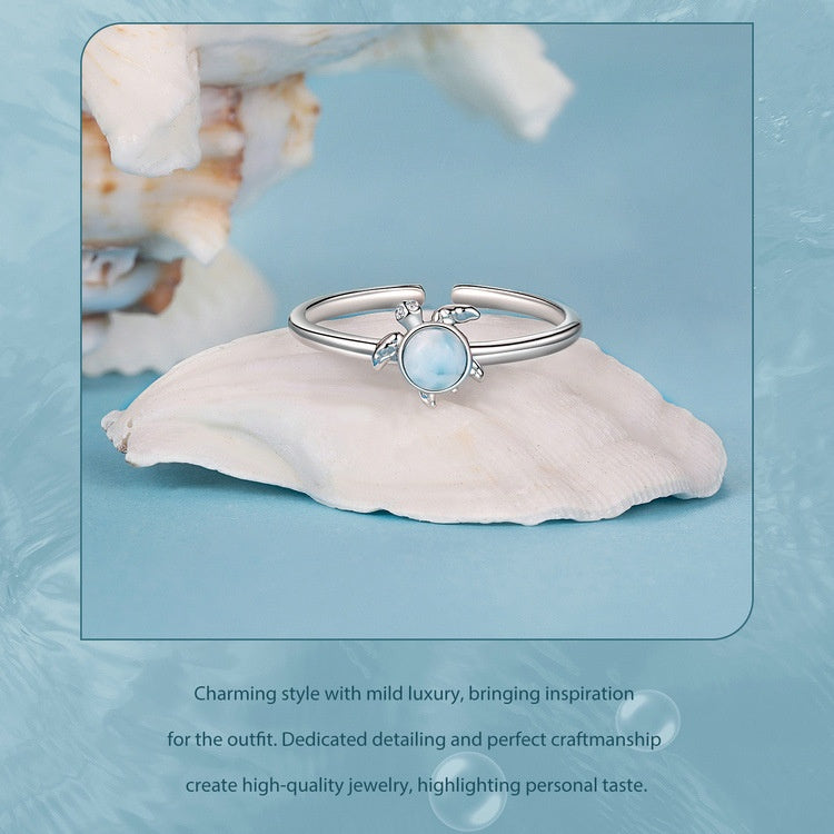 Silver ring with a blue gemstone on a white shell against a light blue background