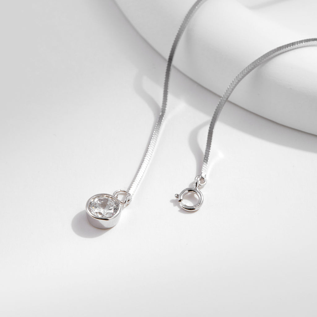 Silver bracelet with a snake chain and round pendant on a light gray background