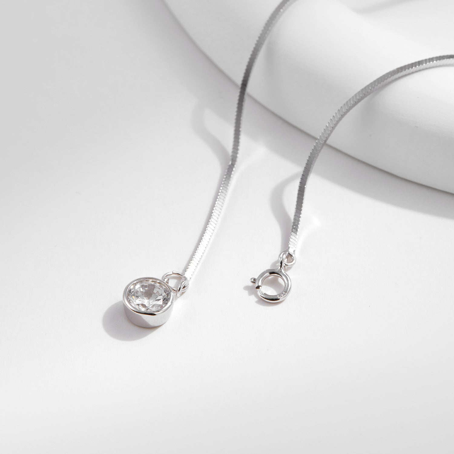 Silver bracelet with a snake chain and round pendant on a light gray background