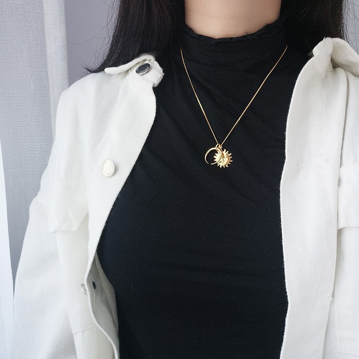 Person wearing a black top and white coat with a gold necklace featuring a sun and a moon pendant.