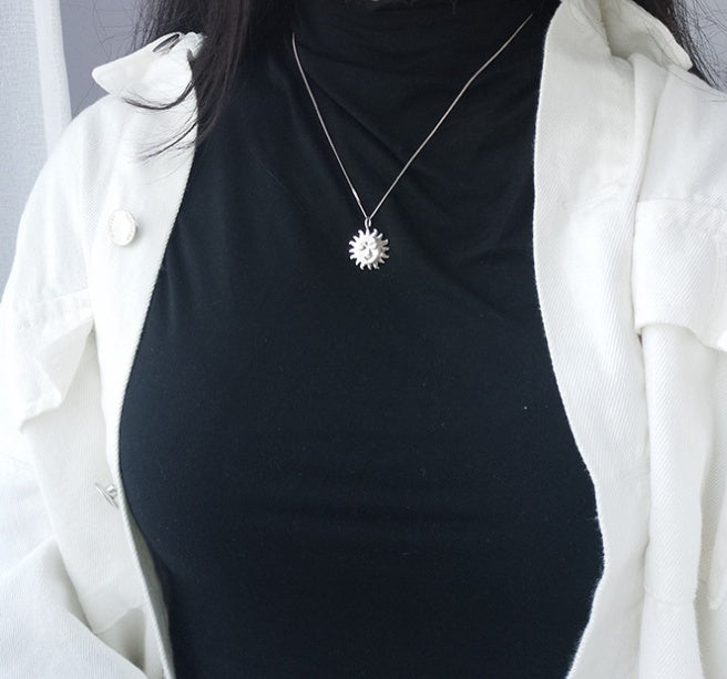 Person wearing a black top and white coat with a silver sun pendant necklace