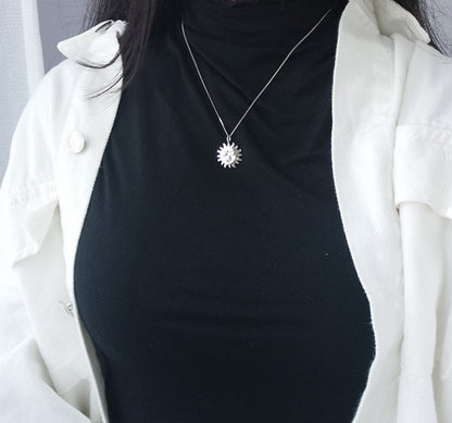 Person wearing a black top and white coat with a silver sun pendant necklace