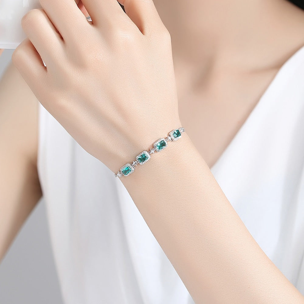 Bracelet with green emerald gemstones on a person's wrist against a white background