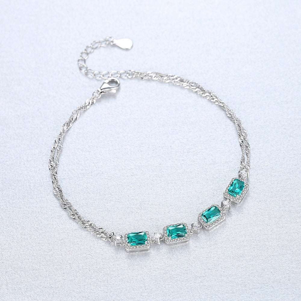 Silver bracelet with green emerald stones on a grey background