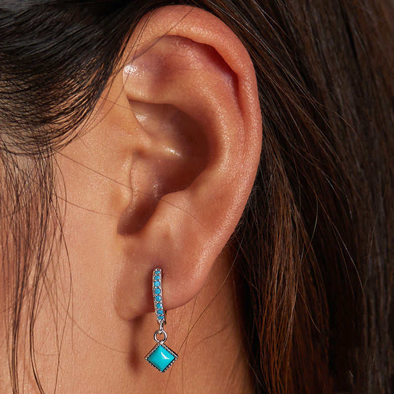 Close-up of an ear wearing a turquoise earring with a diamond-shaped center.