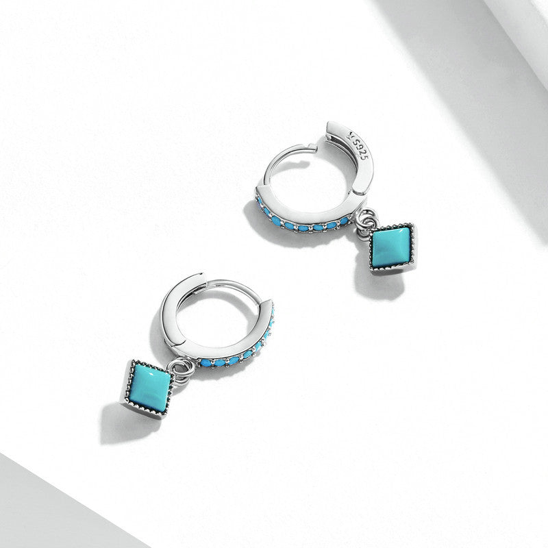 Silver hoop earrings with turquoise square charms on a white background
