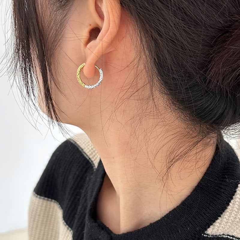 Close-up of a person wearing a two tone gold and silver hoop earring.