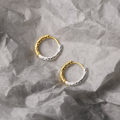 Two tone gold and silver hoop earrings on a textured gray surface