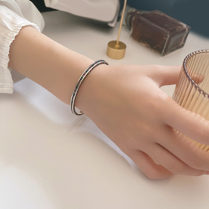Close-up of a hand wearing a silver bracelet with multicolor stones on a light surface.