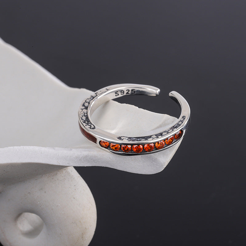 Silver ring with orange stones on a white stand against a dark background