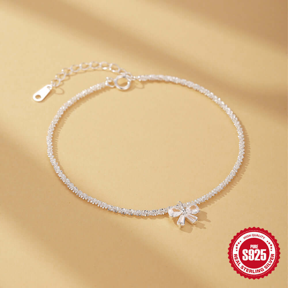 Silver anklet with a bow charm on a beige background, featuring a '925 Sterling Silver' stamp.