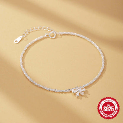 Silver anklet with a bow charm on a beige background, featuring a '925 Sterling Silver' stamp.