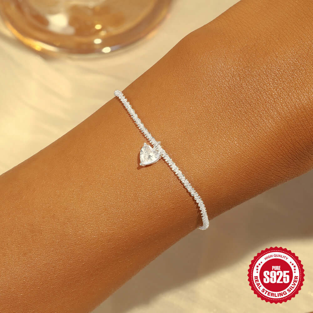 Silver bracelet with a heart-shaped charm on a wrist, with a '925 Sterling Silver' stamp in the corner.