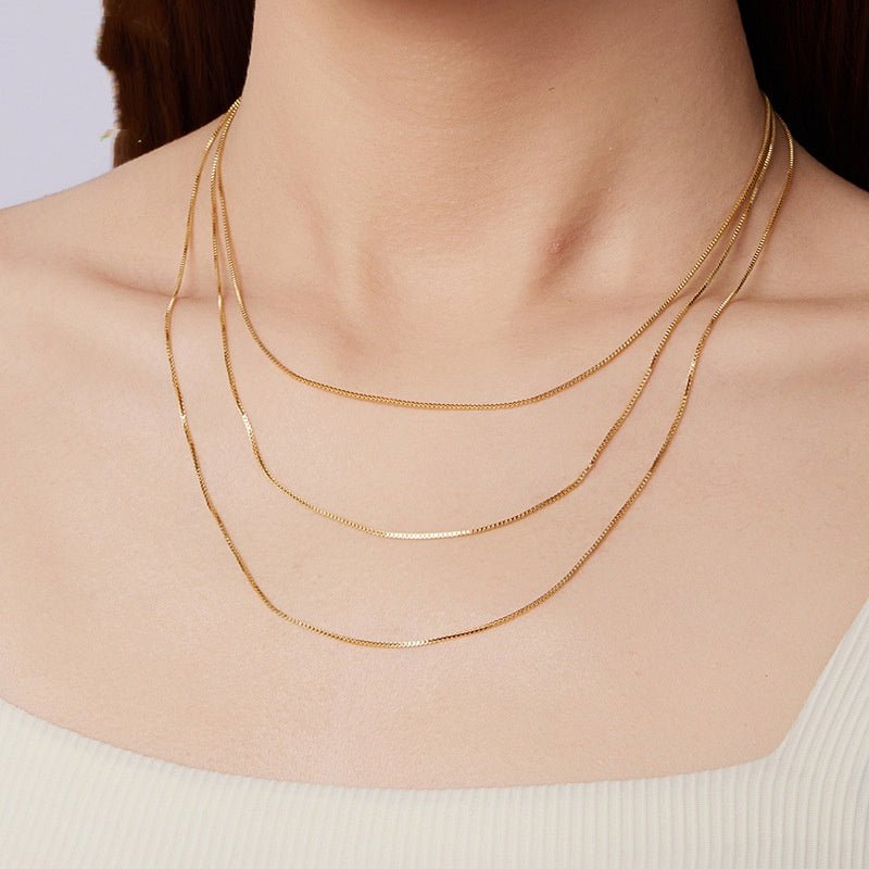 Gold box necklaces on a person's neck against a neutral background