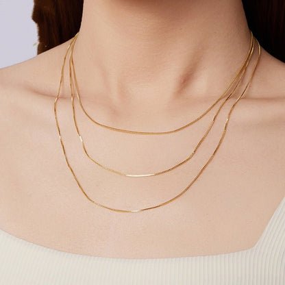 Gold box necklaces on a person's neck against a neutral background