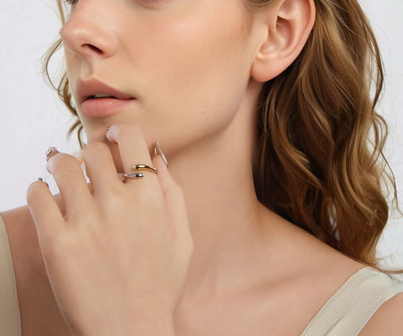 Close-up of a woman wearing droplet ring on her finger against a neutral background