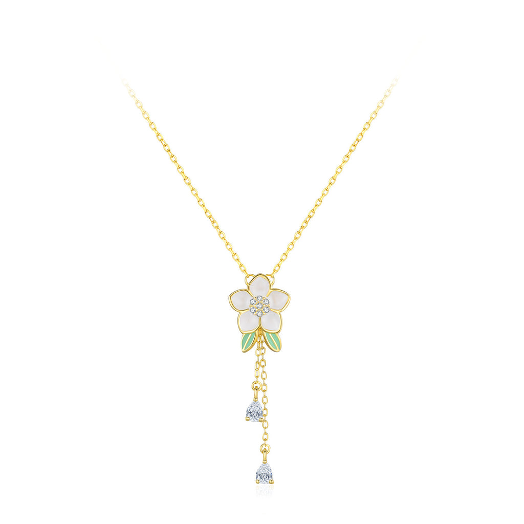 Gold necklace with a white flower pendant on a white background.