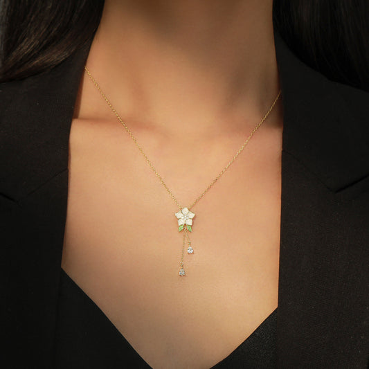 Gold necklace with a floral pendant on a person wearing a black outfit.