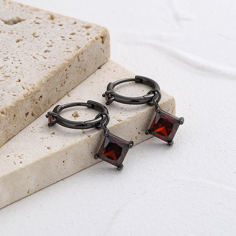 Pair of black hoop earrings with red gemstones on a light stone surface