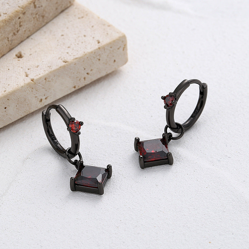 Black hoop earrings with red gemstones on a light surface