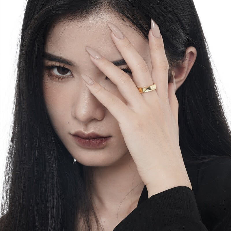 Woman with a gold hexagonal ring on her finger, holding her hand to her face.