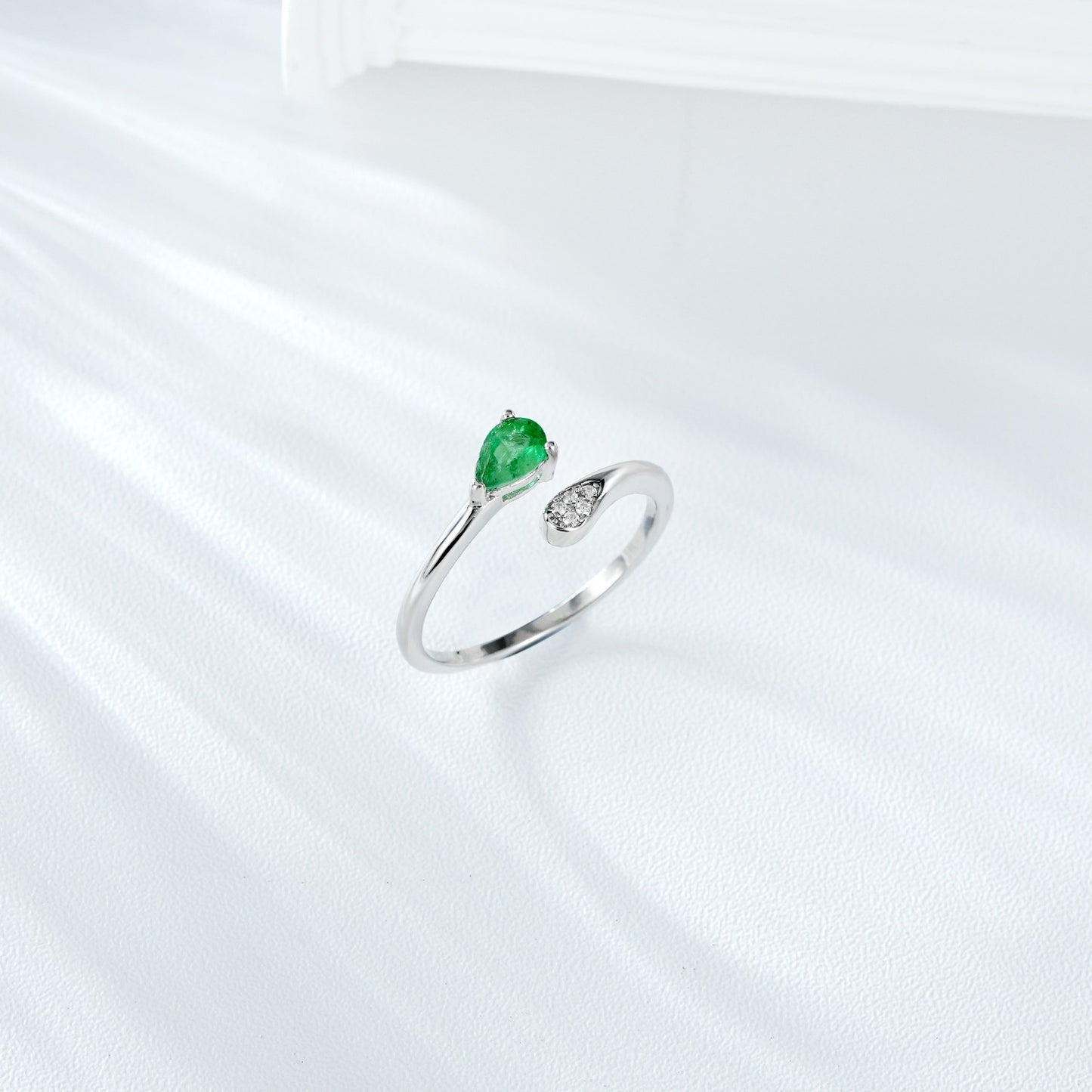 Silver ring with a green emerald gemstone and small zircon diamonds on a white background