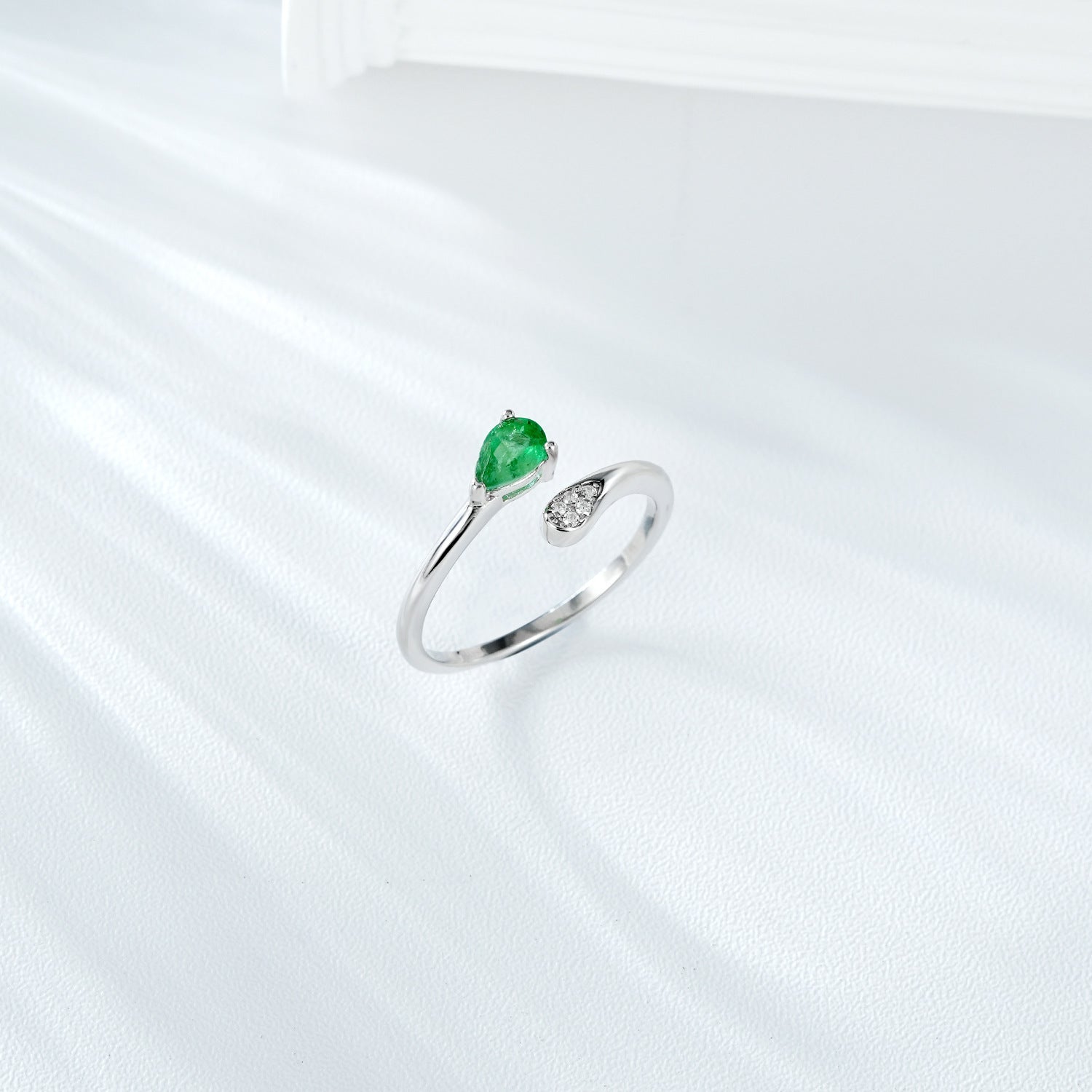 Silver ring with a green emerald gemstone and small zircon diamonds on a white background