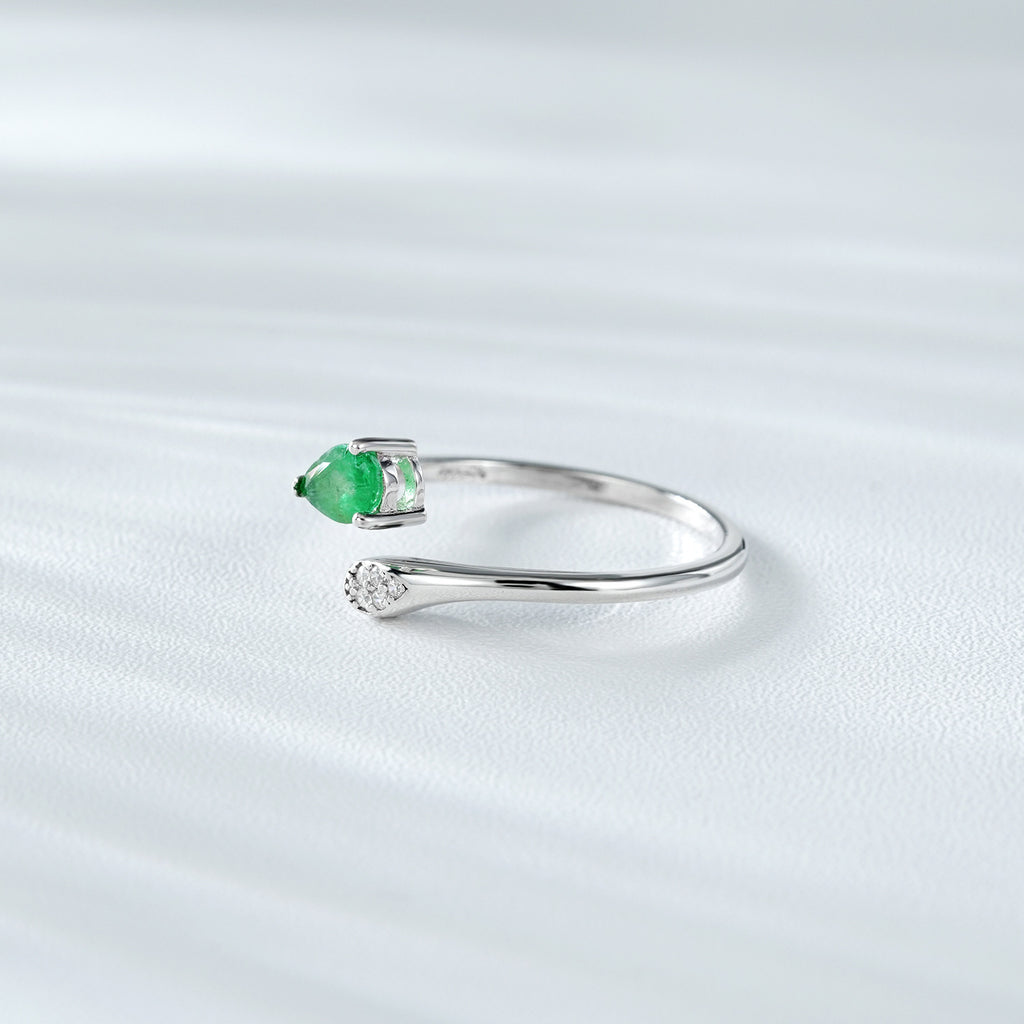 Silver ring with a green emerald gemstone and small zircon diamonds on a white background standing in the side.