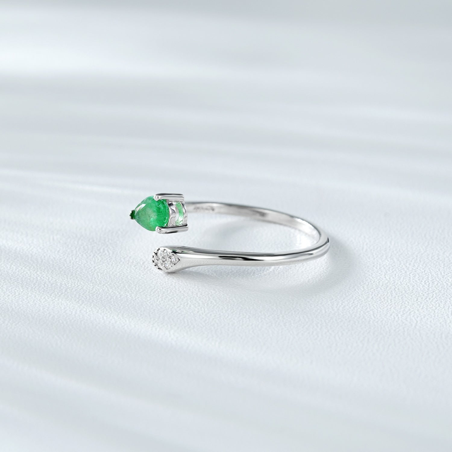 Silver ring with a green emerald gemstone and small zircon diamonds on a white background standing in the side.