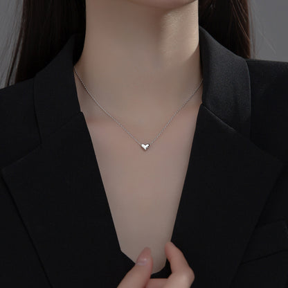 Person wearing a delicate silver necklace with a heart pendant against a dark background