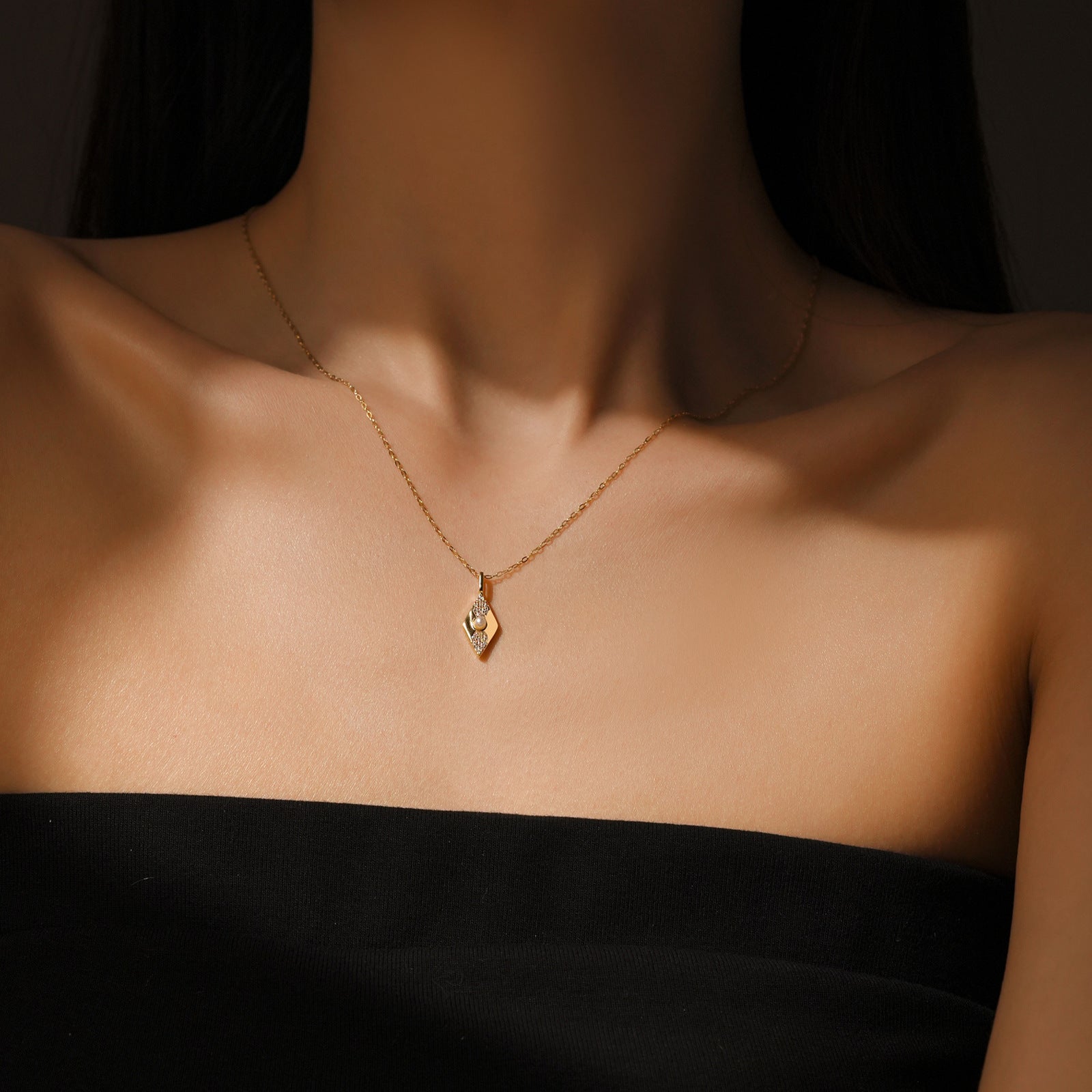 Gold color necklace with a pendant on a person wearing a black top against a dark background.