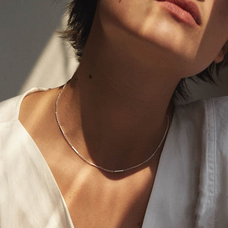 Close-up of a person wearing a delicate  clavicle necklace with a neutral background