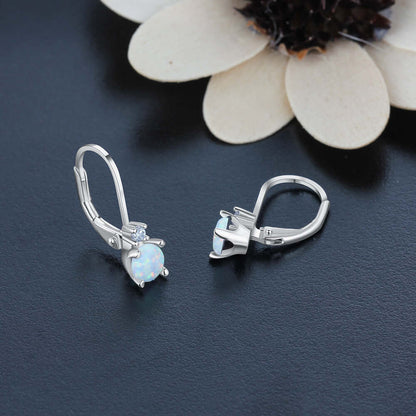 Silver earrings with gemstones on a dark surface with a white flower.