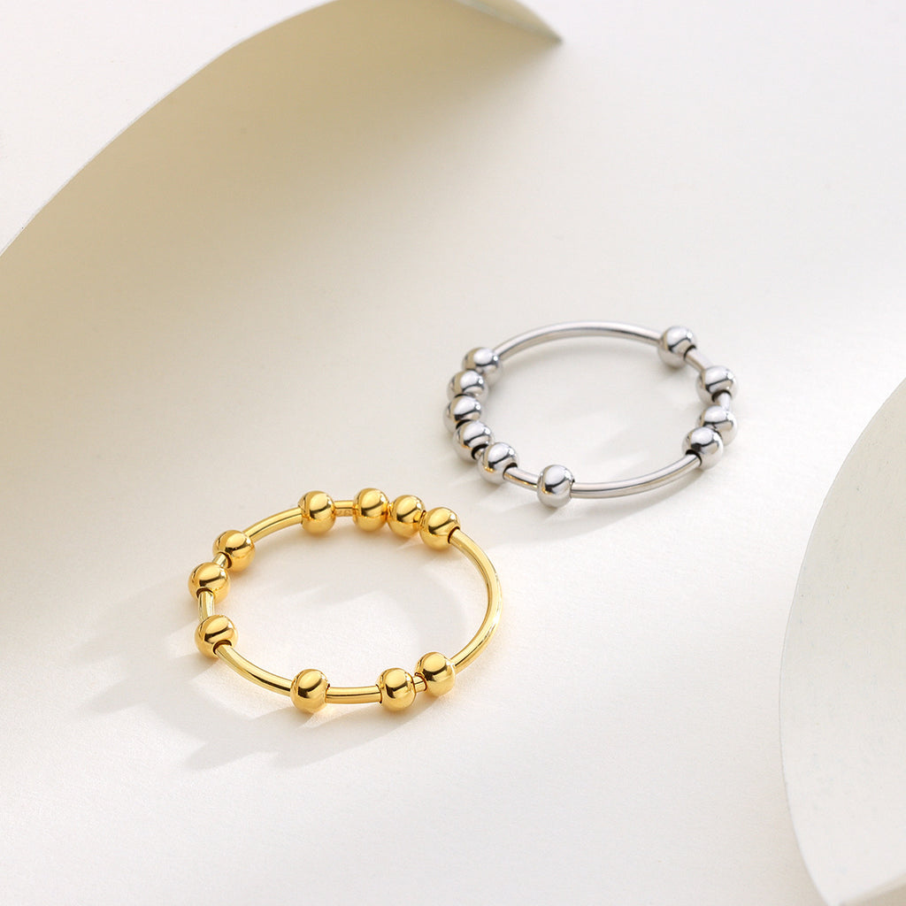 Pair of 925 sterling silver beaded fidget rings, one in gold and one in silver, resting on a white, textured surface.